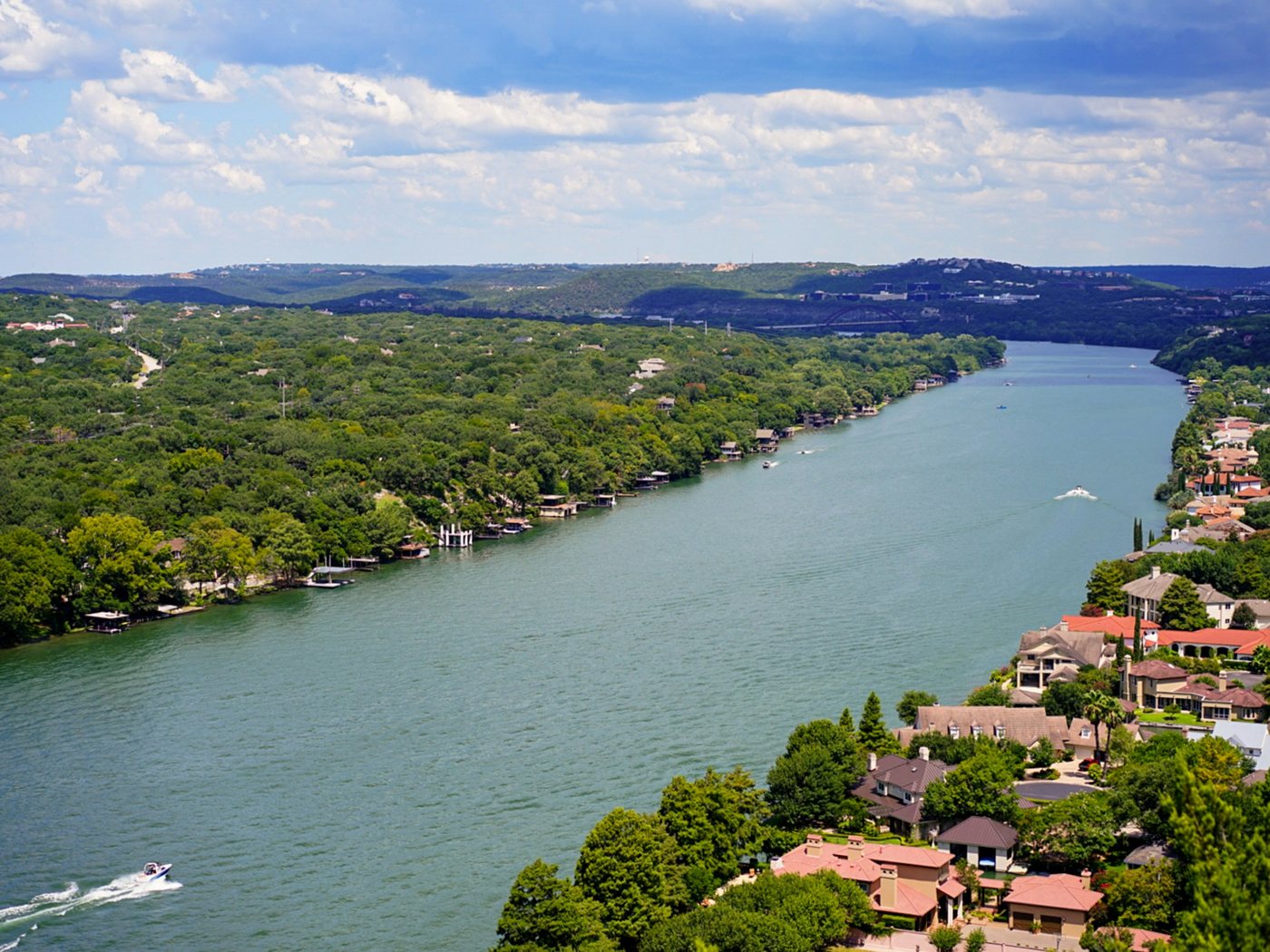 The Colorado River winds through the green hills west of Austin, with houses among the trees along its banks.