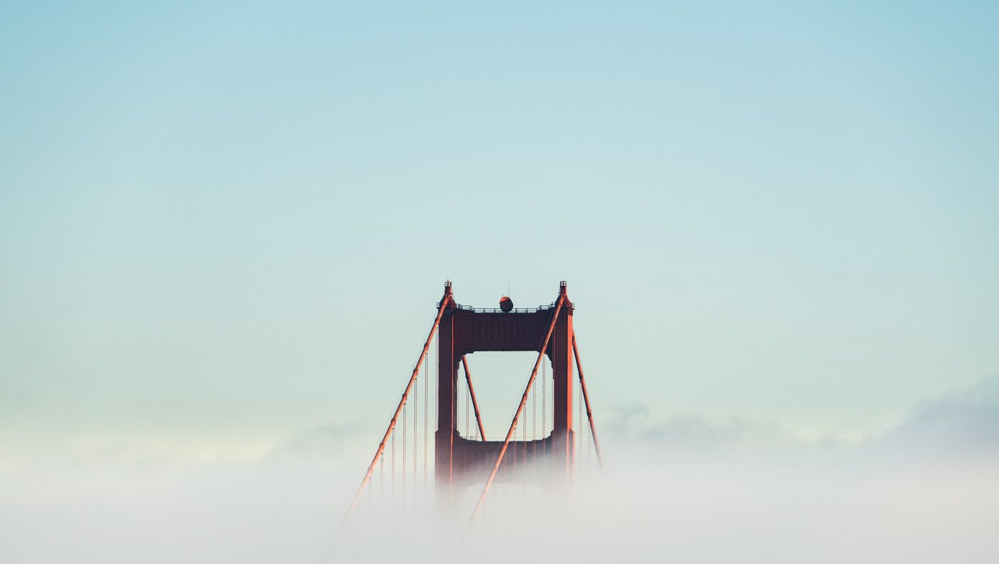 A tower of the Golden Gate Bridge rises out of the fog above San Francisco Bay.